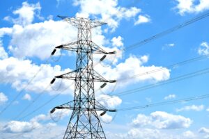 Electricity pylon with high voltage lines set against a vibrant blue sky with clouds.