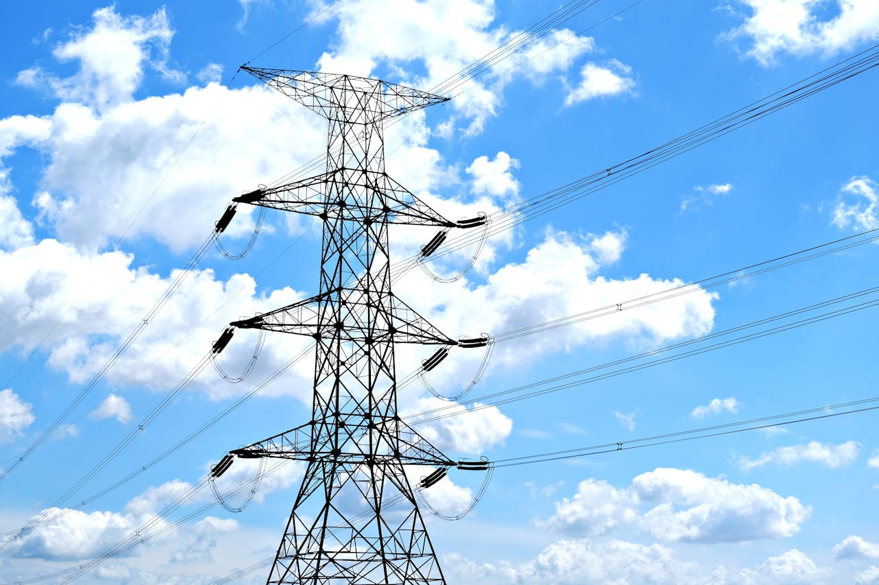 Electricity pylon with high voltage lines set against a vibrant blue sky with clouds.