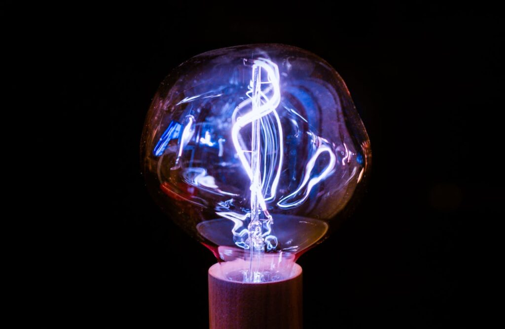 Close-up of a glowing vintage light bulb with an intricate filament design against a dark background.