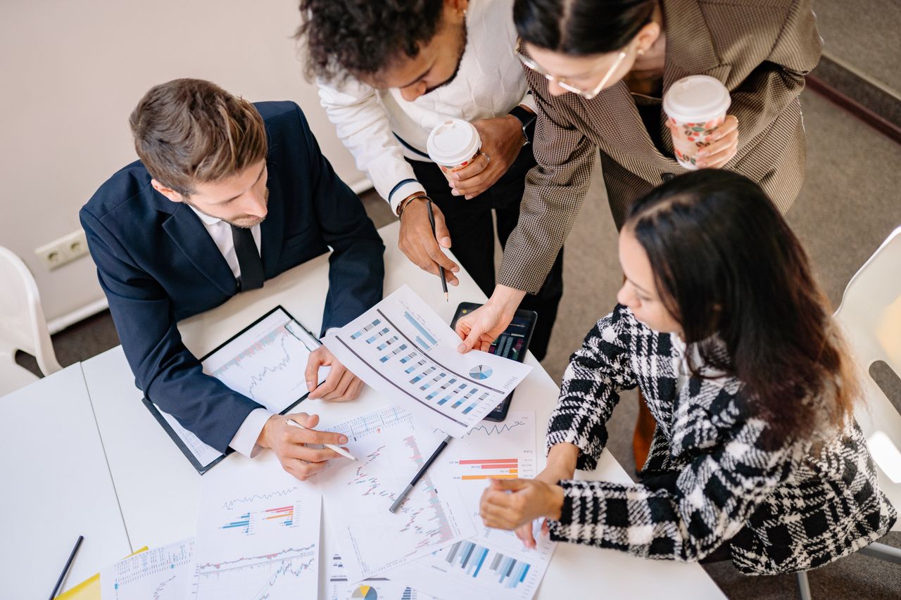 Home A diverse team in business attire collaborates over graphs and charts for a successful project.